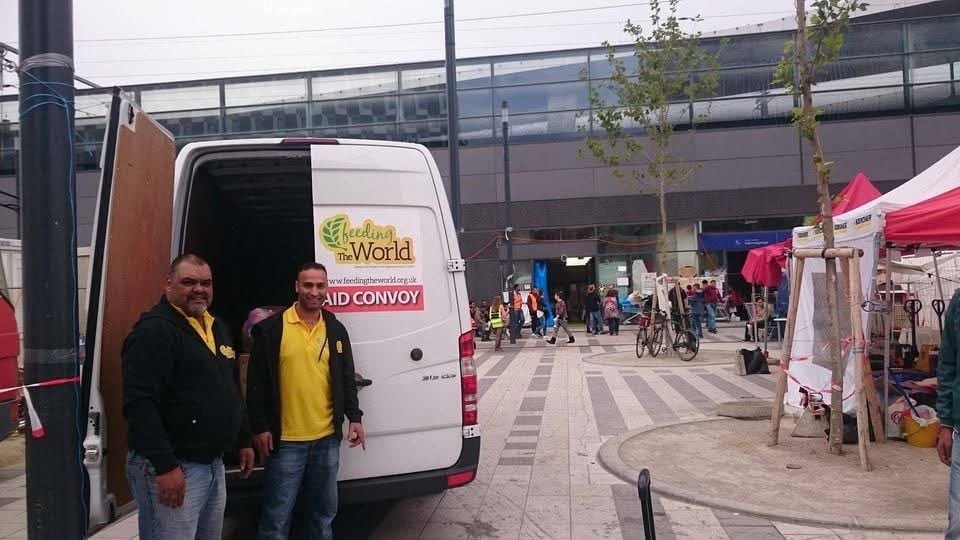 Feeding The World team standing beside the aid convoy van at a distribution point